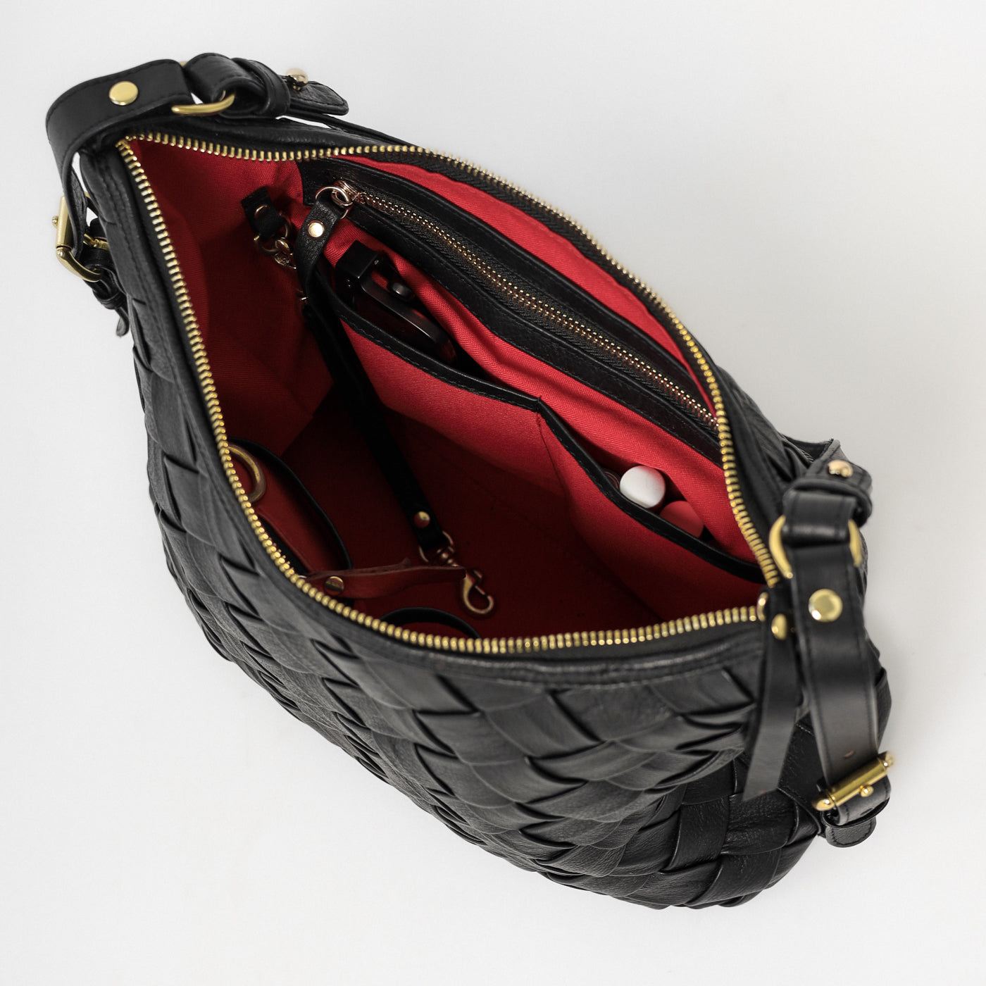 Interior view of the Selena Handwoven black leather bag, showing organized compartments, zip pocket, and red lining with functional storage details.